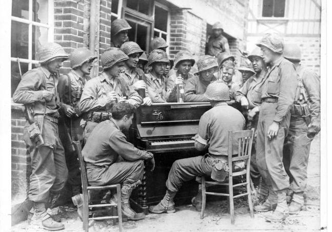 Soldats américains regroupés autour d'un piano, dans une rue de Barenton. 